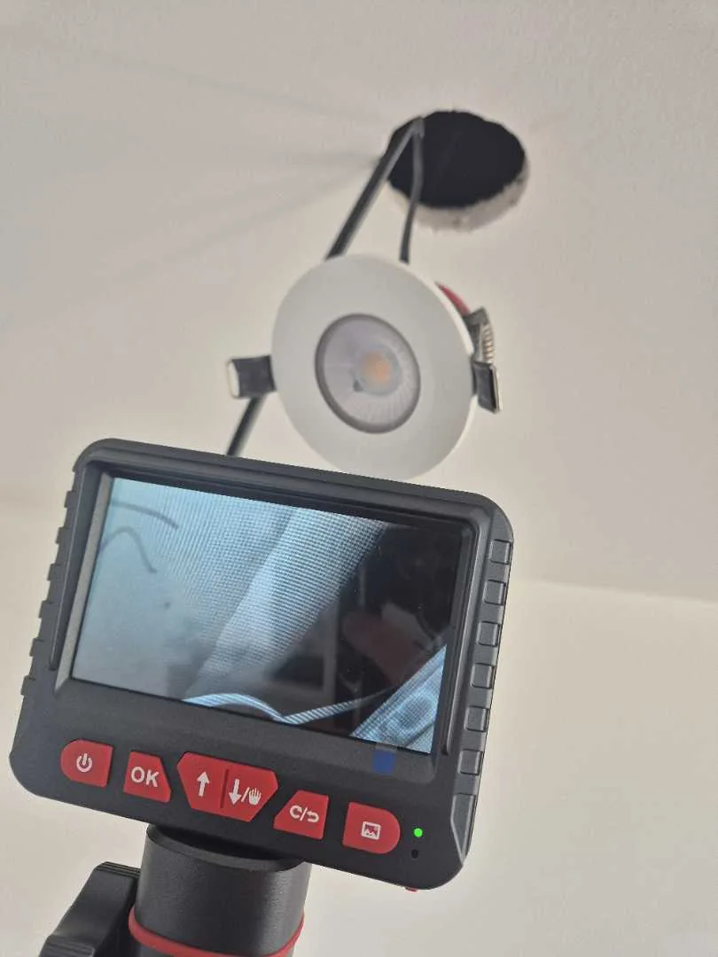 Inspection camera held up to an opening beside a ceiling light